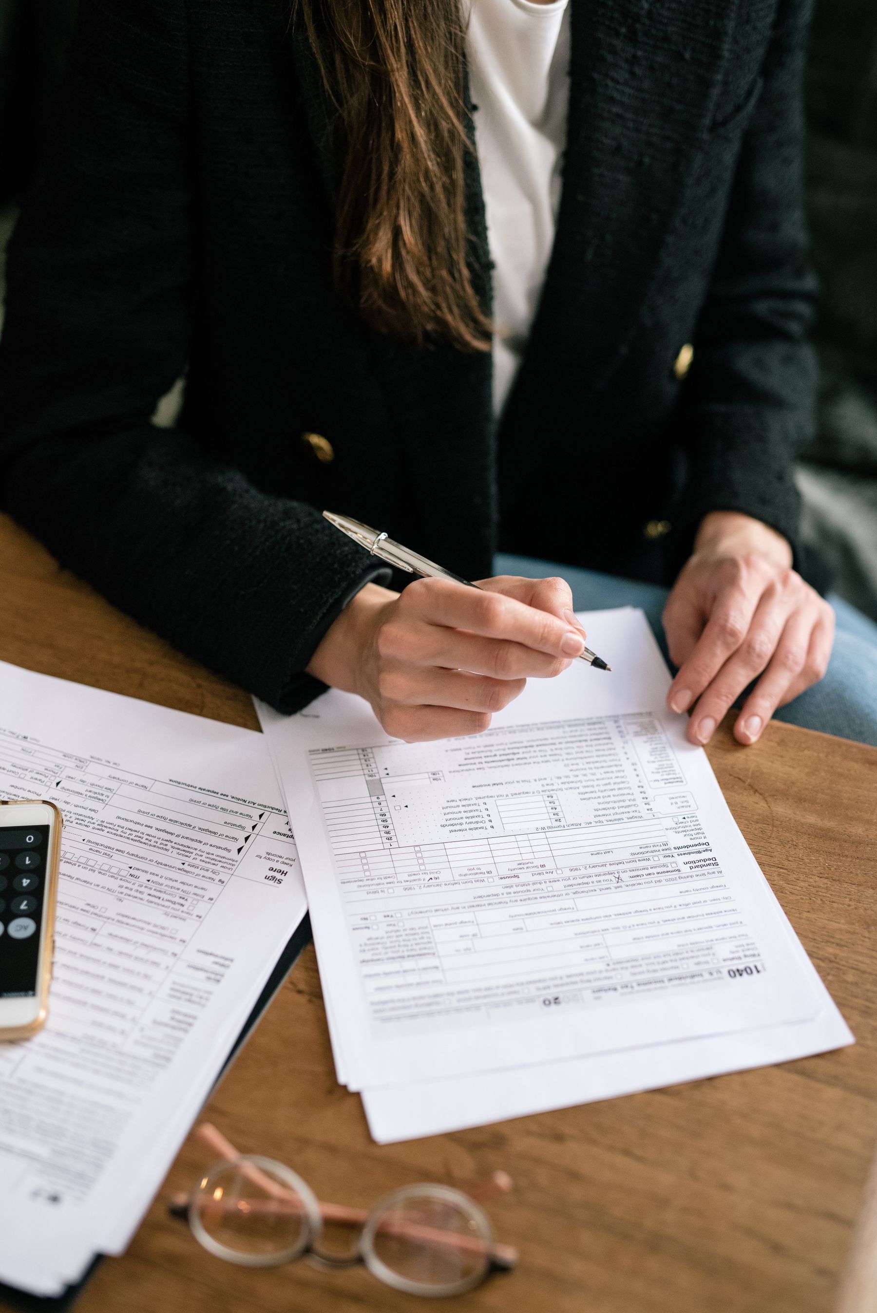 A person reviewing financial paperwork with a pen at a wooden desk