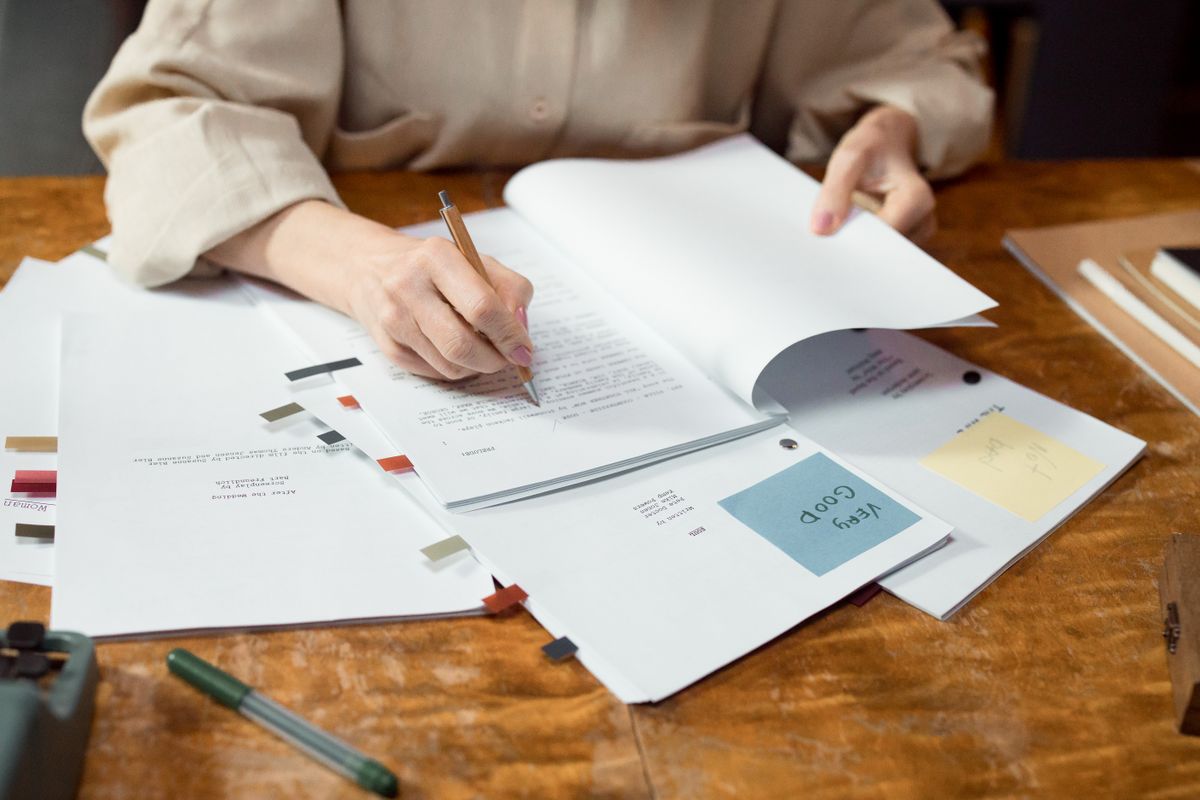 Hands reviewing and annotating printed pages at a wooden desk
